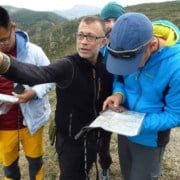 Kaart en kmpas gebruik in de praktijk Ga op avontuur met een navigatietocht in de bergen! Een groep van vier wandelaars demonstreert het gebruik van kaart en kompas in de praktijk. Ze zijn gekleed in outdoor kleding en omringd door groene heuvels en bomen. Beleef de natuur en leer navigeren als een pro!
