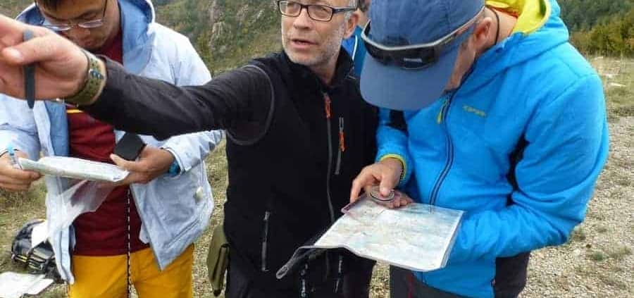 Ga op avontuur met een navigatietocht in de bergen! Een groep van vier wandelaars demonstreert het gebruik van kaart en kompas in de praktijk. Ze zijn gekleed in outdoor kleding en omringd door groene heuvels en bomen. Beleef de natuur en leer navigeren als een pro!