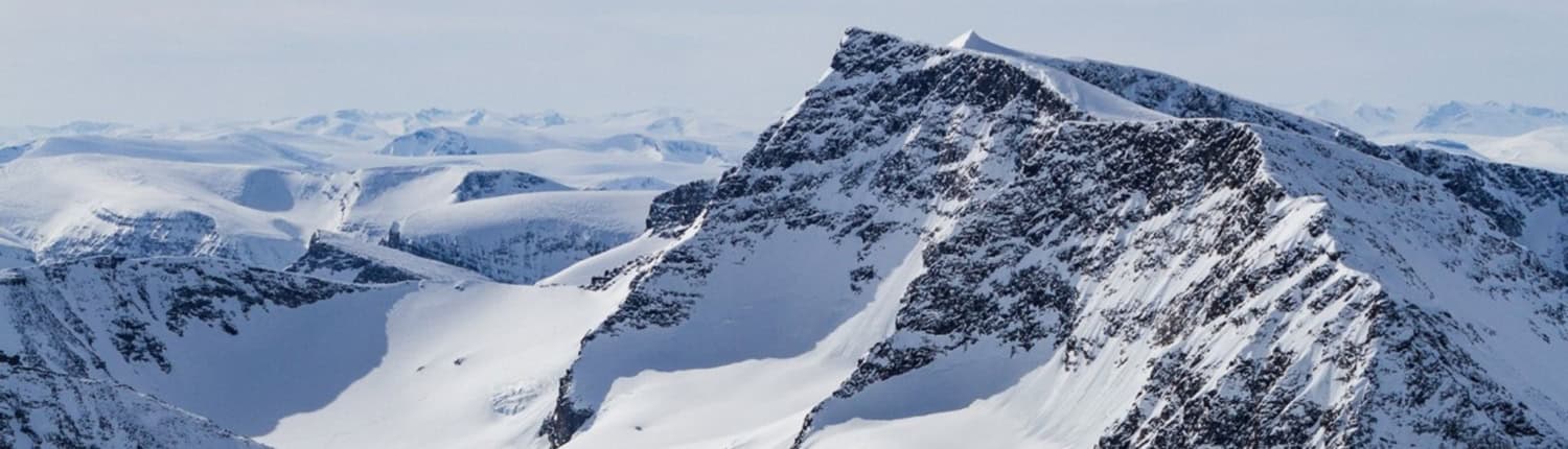 Met sneeuw bedekte bergtoppen tegen een heldere hemel met ruige hellingen en rotspartijen zichtbaar, die doen denken aan Kebnekaise onder het noorderlicht.