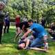 Studio Baak on the Outdoor First Aid Essentials in the Netherlands 5 Een groep mensen traint zelfverdedigingstechnieken in de buitenlucht. Op de voorgrond demonstreert een instructeur een manoeuvre op een cursist die op de grond ligt. Dit lijkt op een Outdoor EHBO-workshop waar volwassenen actief meedoen en toekijken. Omringd door bomen en dicht bij een voetbaldoel, beleef je hier avontuur en leer je essentiële vaardigheden in de frisse buitenlucht.