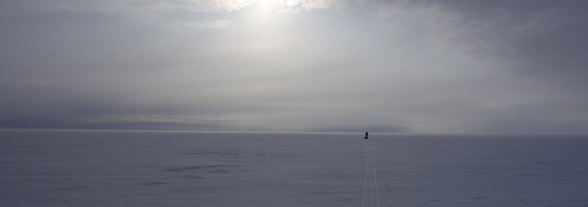 Rustige sneeuwvlakte met enkelspoor en een persoon in de verte tijdens bewolkt weer in de Arctic.