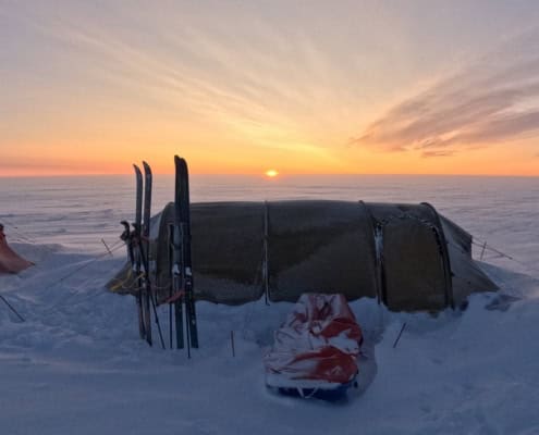 Preparing for an expedition: packing list for a Greenland adventure 1 Schotel onder een polarzon met hoogteverschil, skispullen klaar voor een avontuur in de sneeuw, bij zonsondergang in de Arctic.