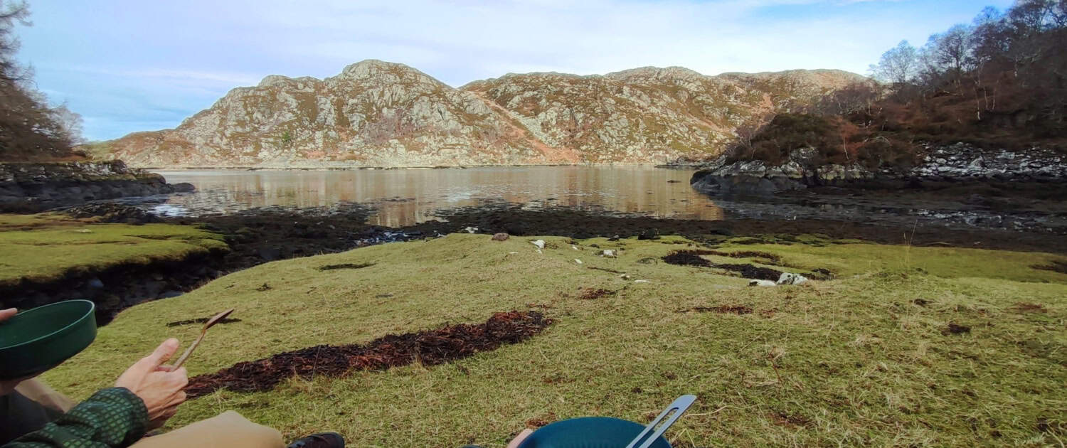 Rustige rivier in de natuur met twee mensen die genieten van een picknick op het gras.