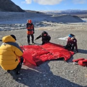 Team pitching a tent in a Greenland environment with ice and mountains in the background.