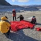 Team pitching a tent in a Greenland environment with ice and mountains in the background.
