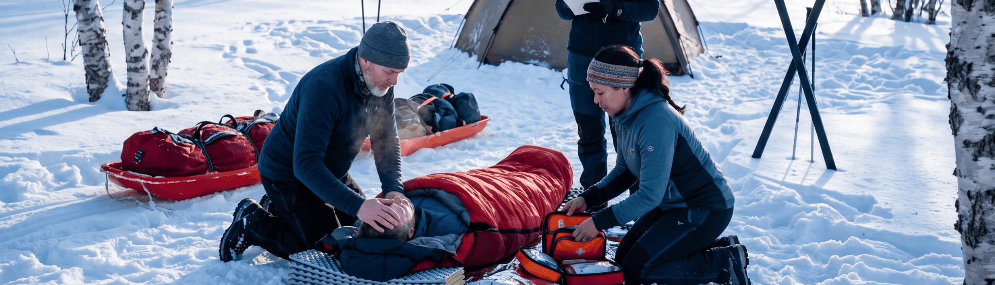 Avontuurlijke wintercamping: twee mensen bieden hulp bij een tent tussen berkenbomen en uitrusting in een besneeuwd landschap.