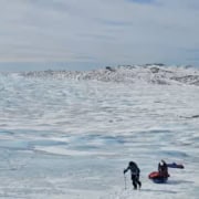 Vast ice plain with hikers and pulks on the Greenland Ice Sheet.