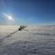 Group hiking across the white landscape of Greenland under a clear blue sky.