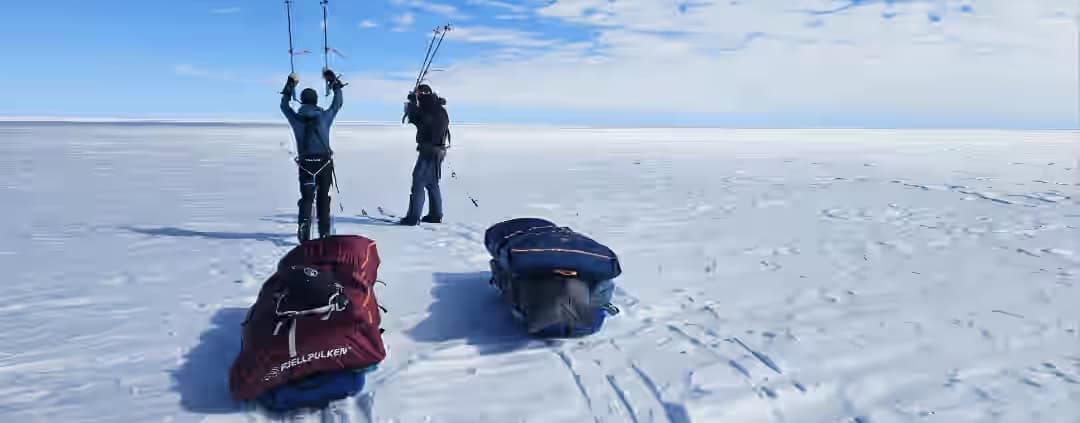 Twee kite surfers op een uitgestrekte sneeuwvlakte met kite-uitrusting.