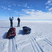 Twee kite surfers op een uitgestrekte sneeuwvlakte met kite-uitrusting.