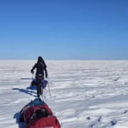 Persoon op sneeuwscooter in uitgestrekte Arctische sneeuwvlakte onder blauwe hemel.