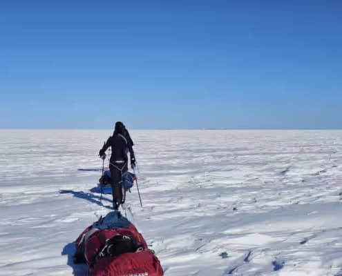 Persoon op sneeuwscooter in uitgestrekte Arctische sneeuwvlakte onder blauwe hemel.