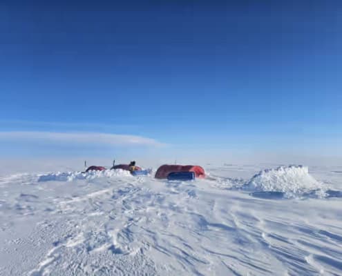 Drie tenten zijn opgezet op de Groenlandse ijskap, voorzien van een sneeuwmuur als bescherming tegen de opkomende storm.