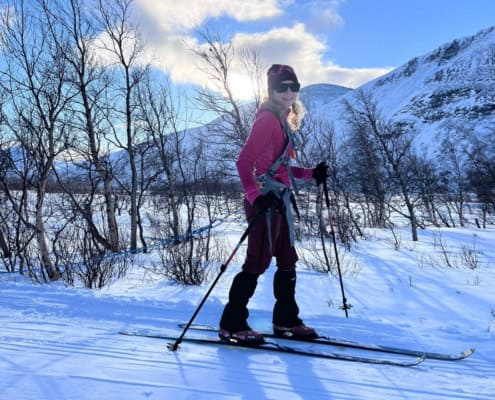 Vrouw skiet in besneeuwd landschap met bergen en bomen op de achtergrond.