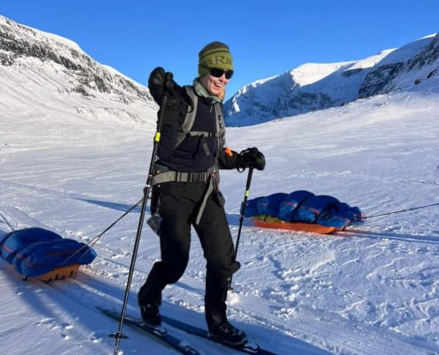 Sneeuwsporter met ski's en slee in de Noorse fjorden, omringd door besneeuwde bergen onder een helde.