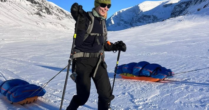 Sneeuwsporter met ski's en slee in de Noorse fjorden, omringd door besneeuwde bergen onder een helde.