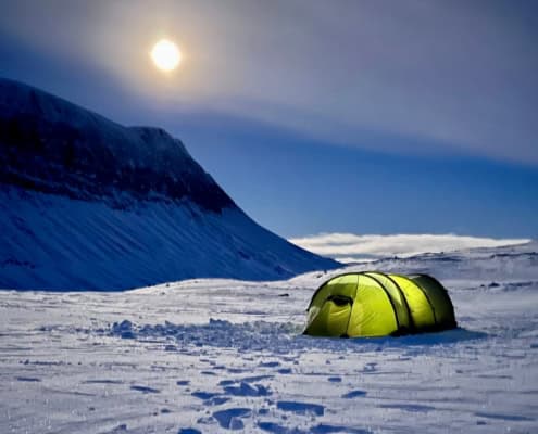Kampeer tent op sneeuw onder volle maan in Arctisch landschap.