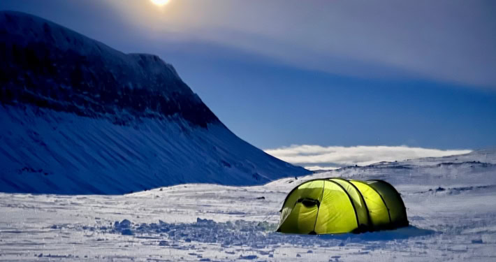 Kampeer tent op sneeuw onder volle maan in Arctisch landschap.
