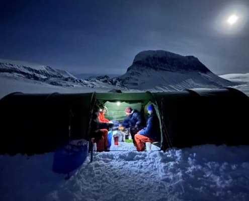 Sneeuwkamp met mensen die genieten van een avond in de sneeuw onder de maan.