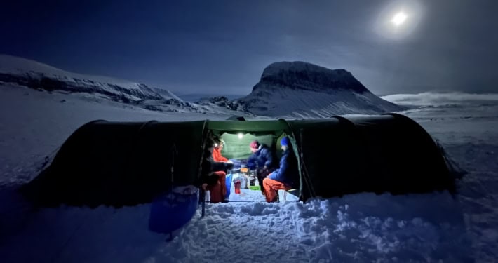 Sneeuwkamp met mensen die genieten van een avond in de sneeuw onder de maan.